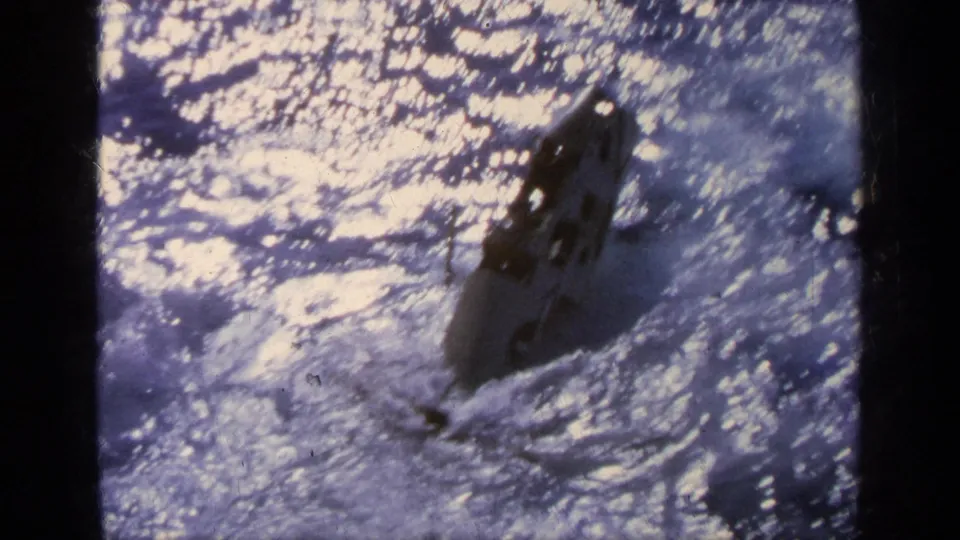 The jet appears nose-down in sunlit ocean water, with spray and glare surrounding the impact area.