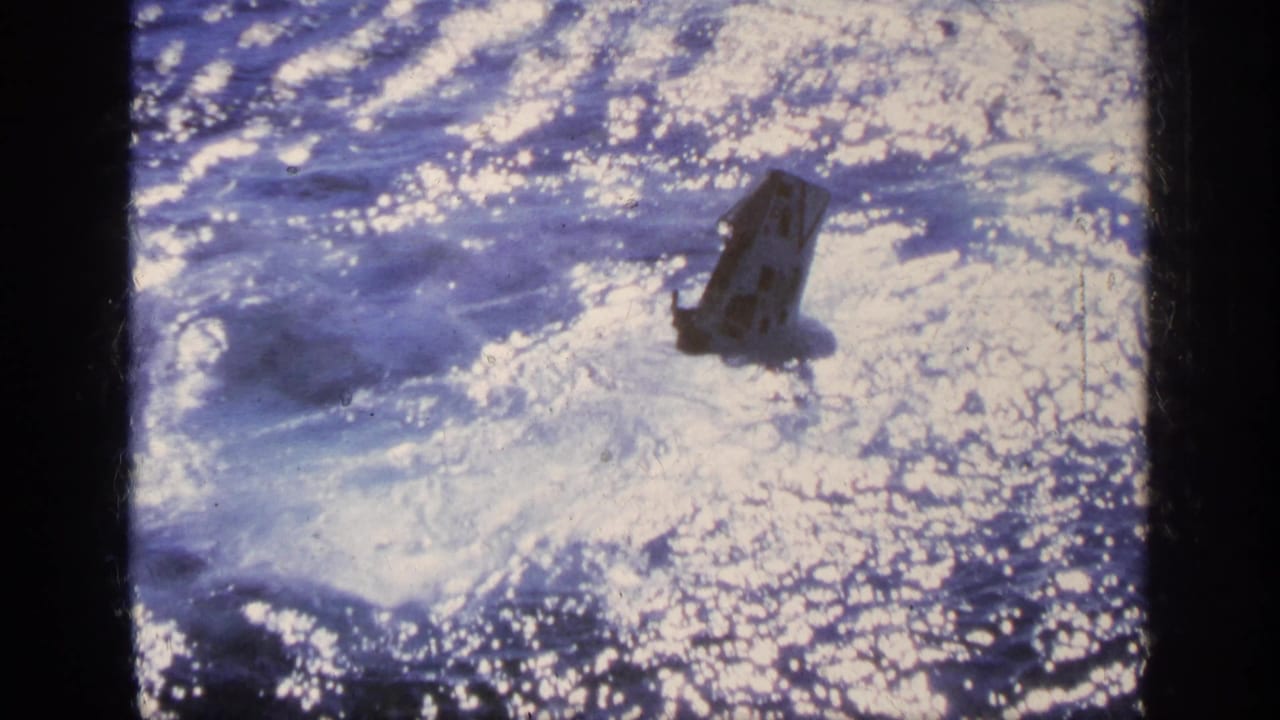 1963 Greece 8mm frame showing a small dark boat pitching amid rough, sunlit blue water and white foam.
