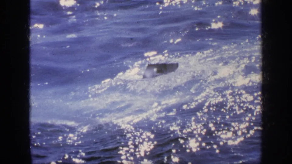 1963 Greece 8mm frame showing the small vessel low in the water as white foam and glare surround it.