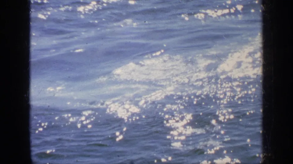 1963 Greece 8mm frame dominated by choppy blue water, white foam and bright reflected sunlight after the boat passes from view.
