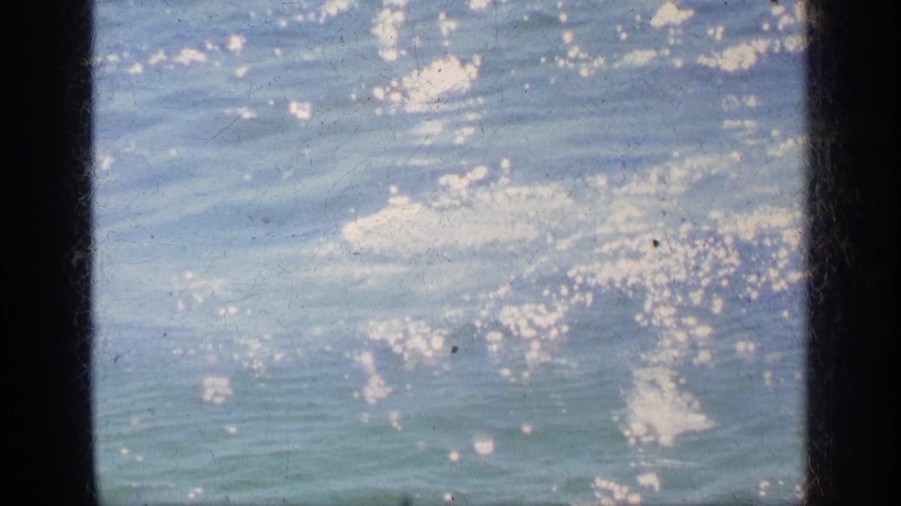 1963 Greece home-movie frame showing shimmering sea water with bright surface swirls and visible 8mm gate borders.