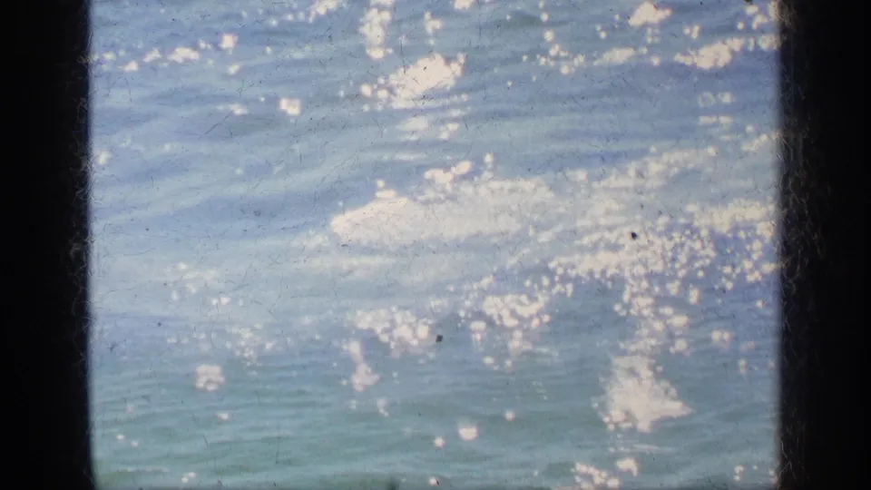 1963 Greece home-movie frame showing shimmering sea water with bright surface swirls and visible 8mm gate borders.