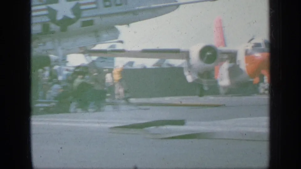 1963 Greece footage appears to show a twin-engine propeller aircraft with orange and white markings on a naval carrier deck, with crew nearby.