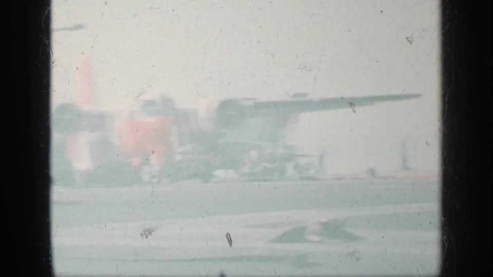 Faded 8mm frame from the 1963 Greece clip showing the same deck aircraft in soft focus with pale exposure and visible film wear.