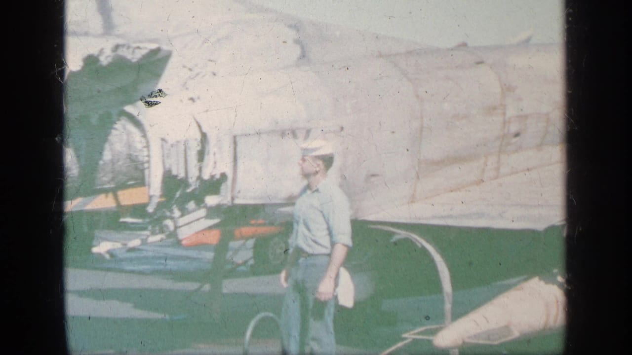 Man in a light shirt and cap standing beside a small aircraft on a tarmac.
