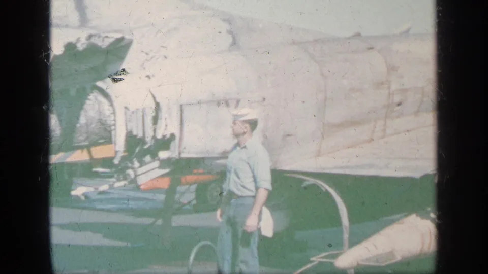 1963 Greece home-movie frame showing a man in a cap near a light aircraft on a bright tarmac.