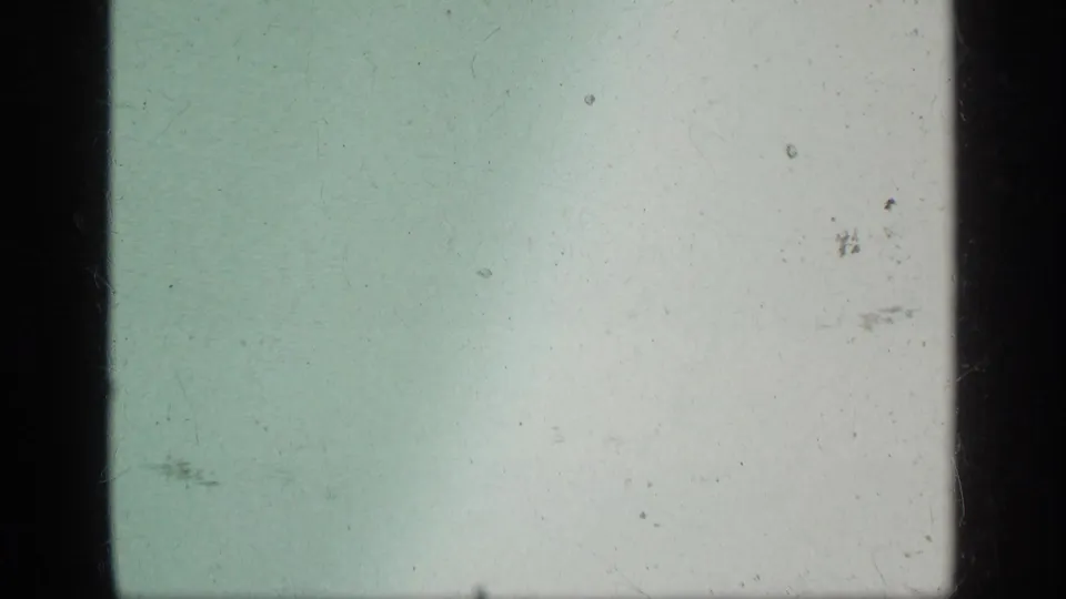 Pale green-blue 8mm frame with minimal visible scene content and pronounced dust and scratches.