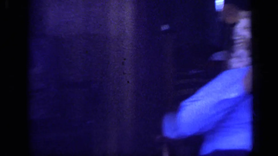 A blurred figure in a blue shirt passes through the frame during the handheld 1968 California interior shot.