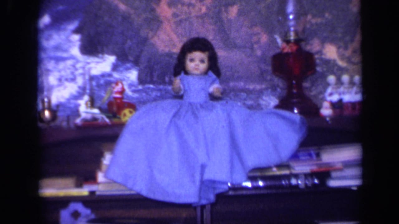 Blue-dressed doll displayed on a shelf with toys, books, and holiday decorations.
