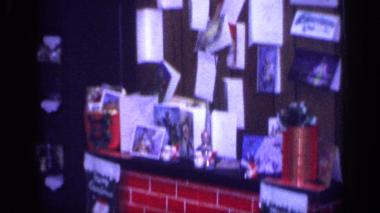 1968 California home-movie frame showing a mantel display with cards, stockings, papers, and small Christmas decorations.
