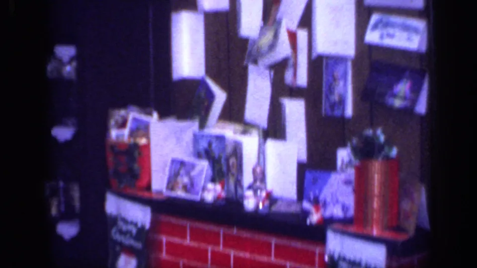 1968 California home-movie frame showing a mantel display with cards, stockings, papers, and small Christmas decorations.