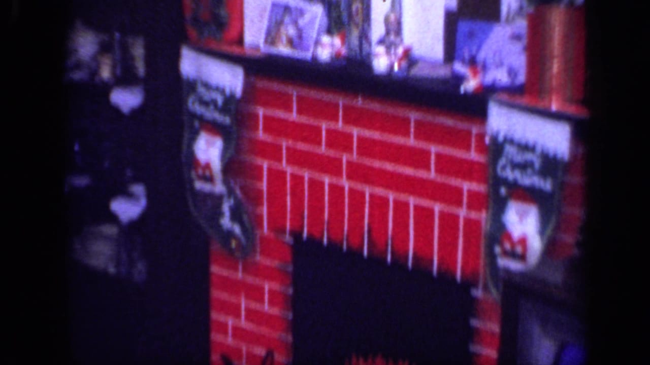 1968 California home-movie frame showing a Christmas fireplace display with stockings, mantel objects, and artificial flames.