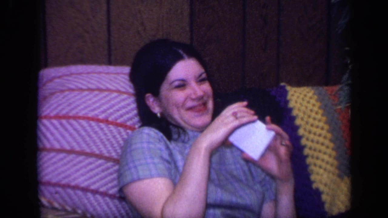 Woman in a plaid dress sits on a sofa holding a small white object.