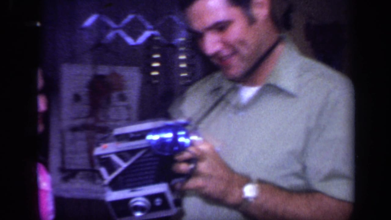 Man in a light shirt holds a glowing blue object near a partially visible woman indoors.