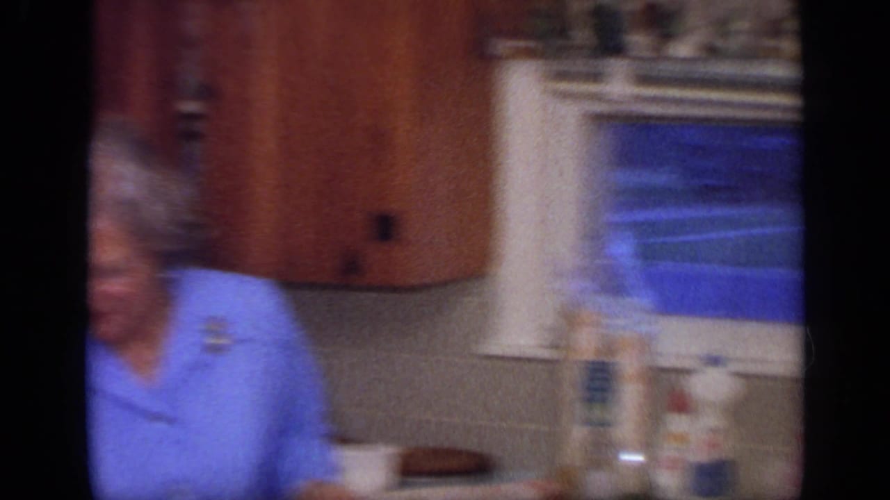 1968 California home-movie frame showing women in a kitchen, with countertop items and a window behind them.