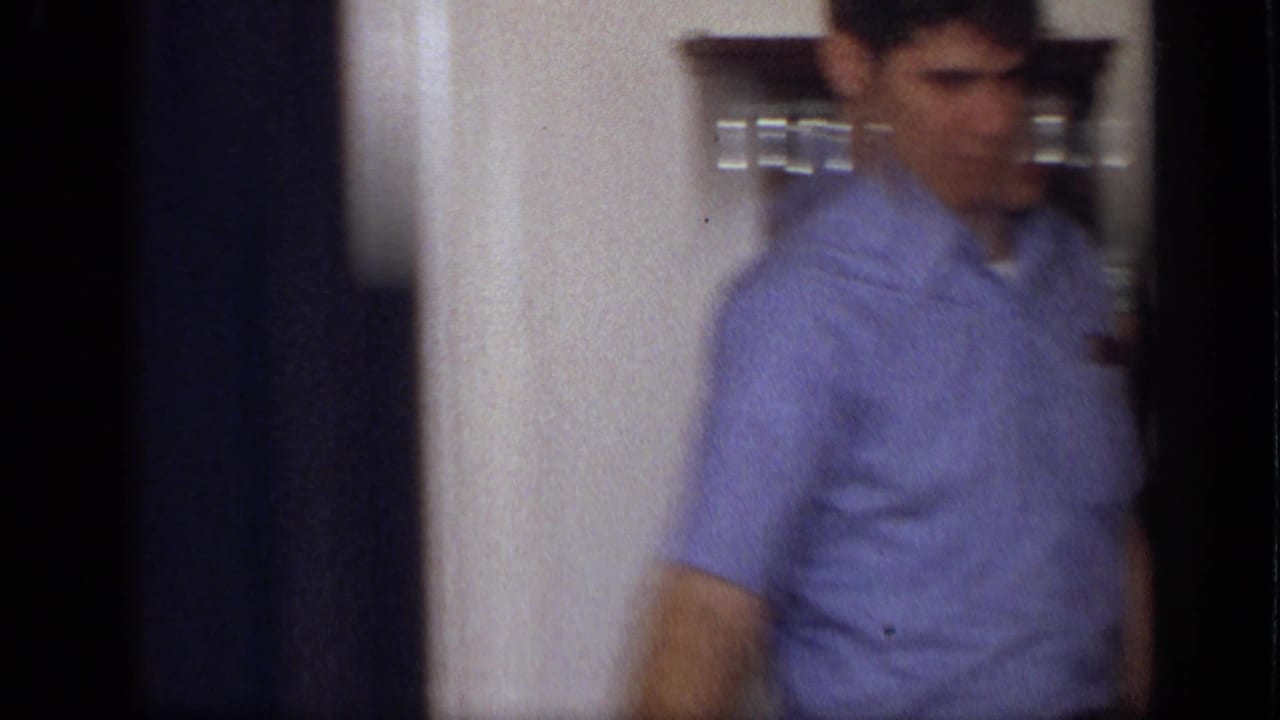 In a 1968 California home kitchen, a young man in a blue short-sleeve shirt moves past a doorway and wall-mounted spice rack.
