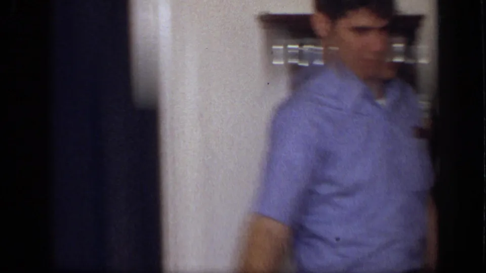 In a 1968 California home kitchen, a young man in a blue short-sleeve shirt moves past a doorway and wall-mounted spice rack.