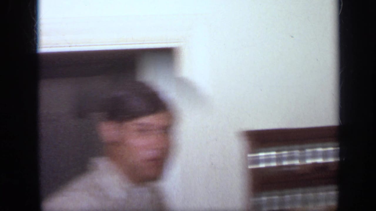 1968 California home-movie frame showing a blurred young man in a striped shirt passing through an interior doorway.