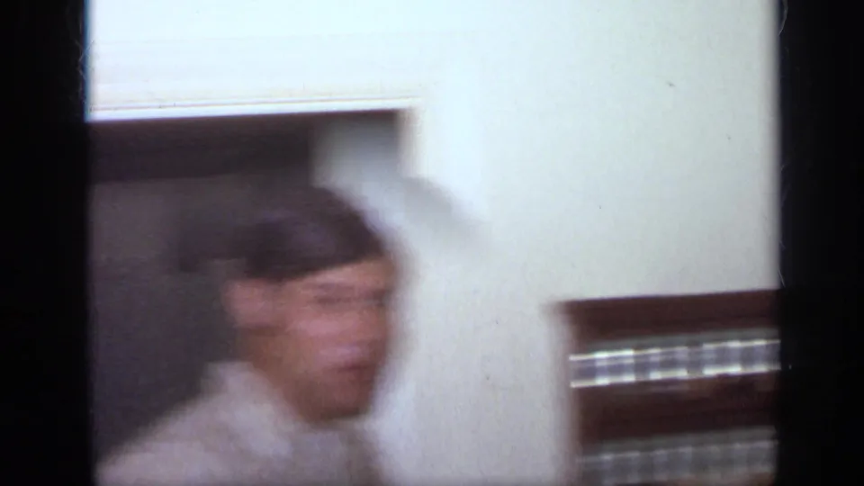 1968 California home-movie frame showing a blurred young man in a striped shirt passing through an interior doorway.