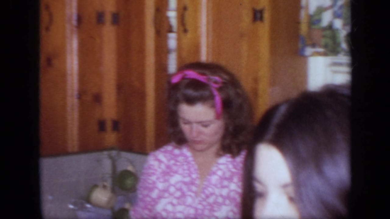Woman in a pink patterned dress standing in a kitchen with wood cabinets.