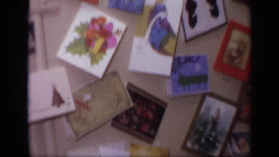 Christmas cards and illustrated postcards are scattered across a home interior surface in the 1968 California holiday footage.