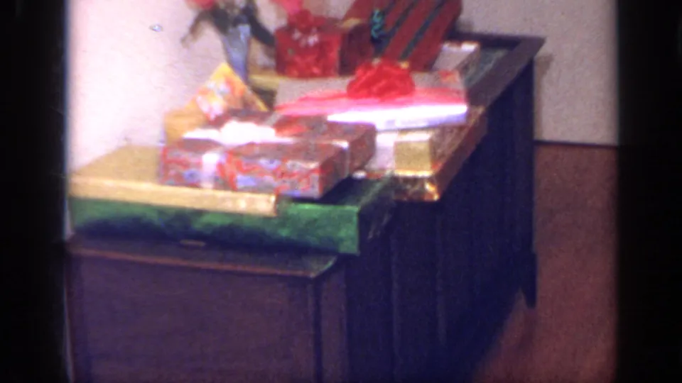 Wrapped holiday presents with bright ribbons and bows are arranged on furniture inside the California home-movie scene.