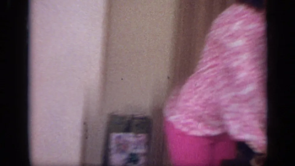 A woman in a pink patterned sweater and matching pants stands partly in frame near a wall in the 1968 California home interior.