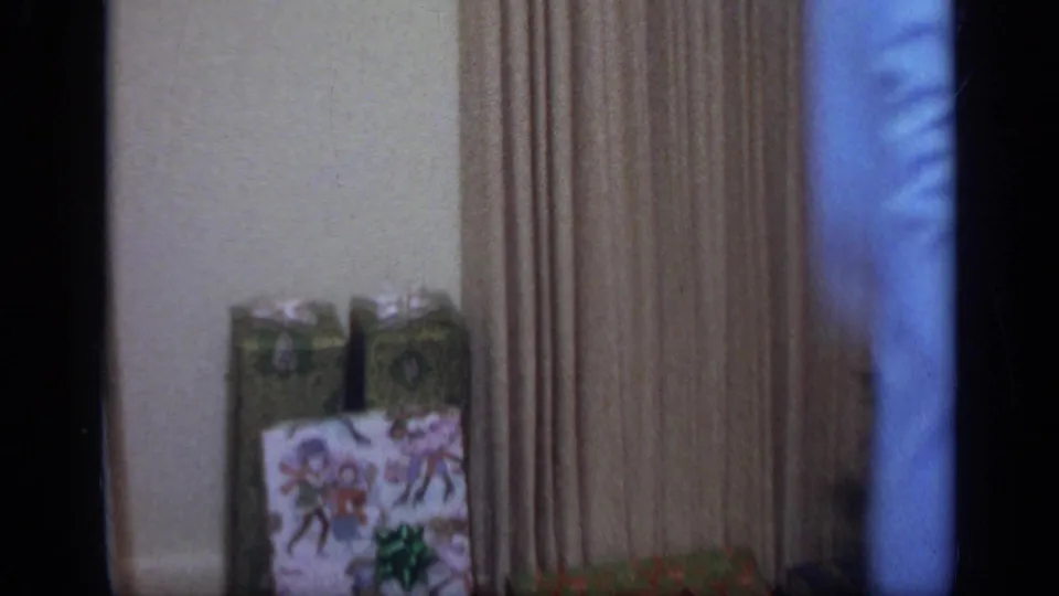 The camera drifts past a wall and curtains toward wrapped holiday gifts near the Christmas tree in a private California interior.
