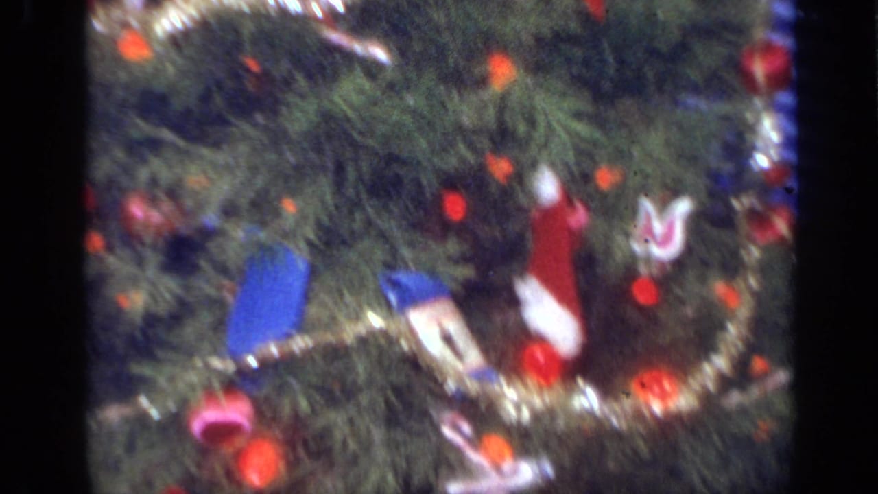 Close 8mm view of a decorated Christmas tree with gold garland, red ornaments and small stocking decorations.