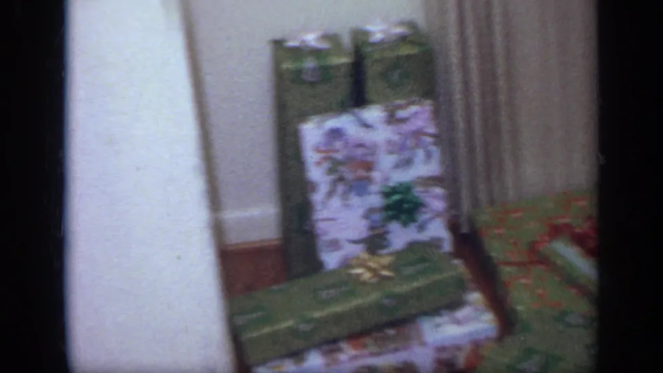 8mm frame showing several wrapped Christmas gifts arranged near a wall and doorway inside a California home.