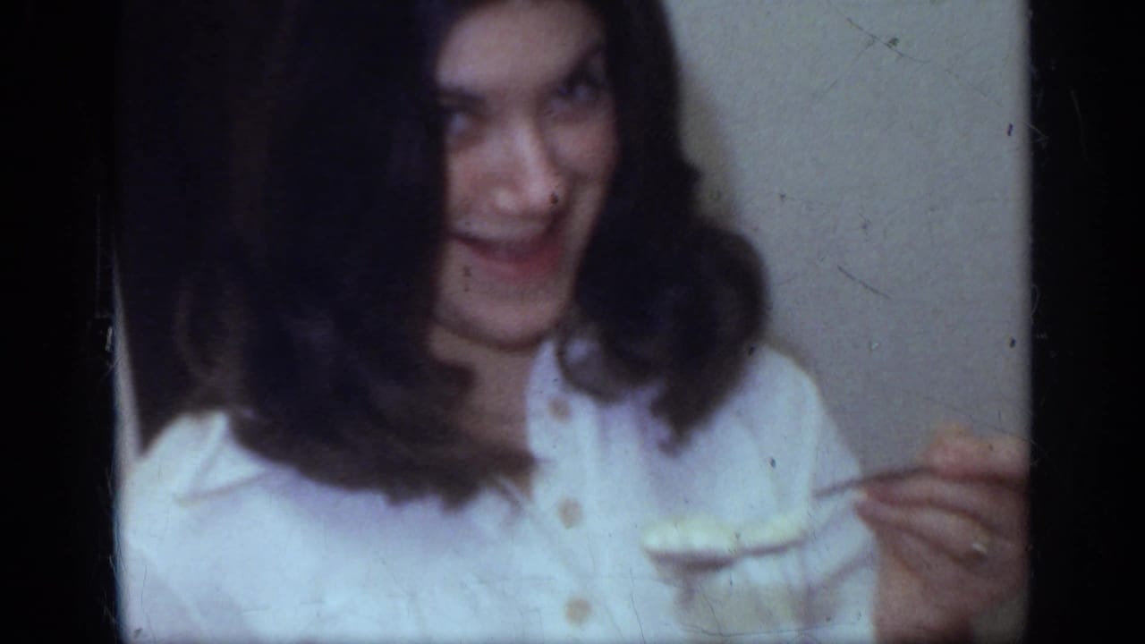 Young woman in a white blouse laughs while seated indoors.
