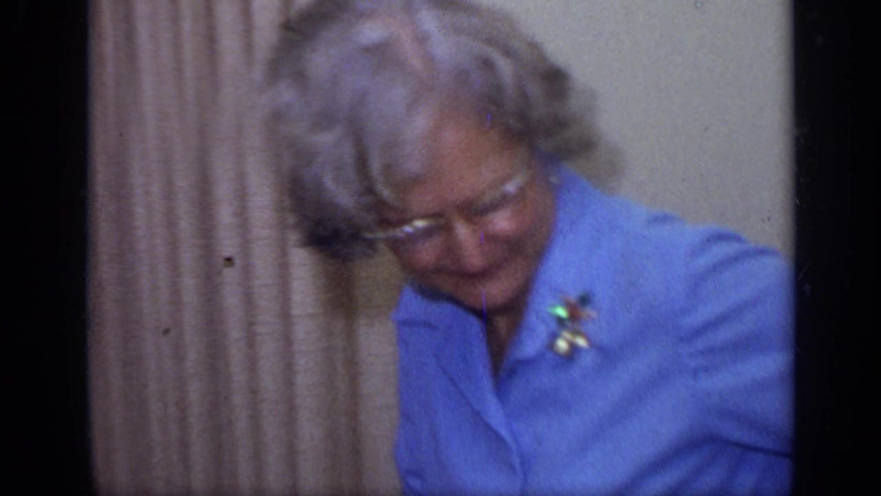 Older woman in glasses looks down while seated indoors.