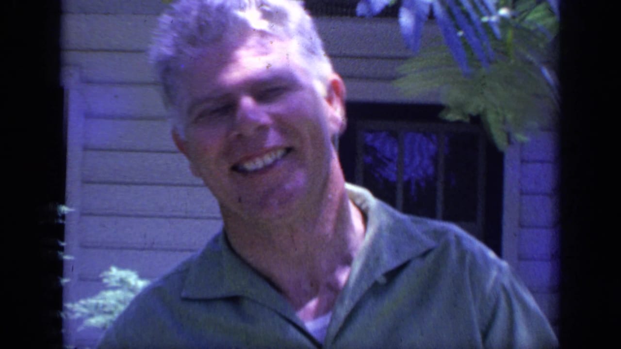 1968 Florida home-movie frame of a smiling adult counselor in a green collared shirt outside a light-sided building.