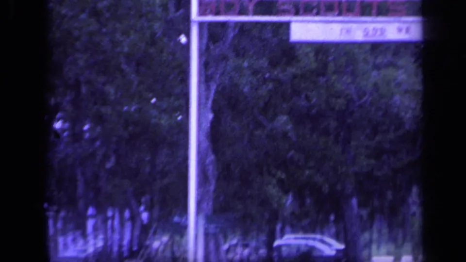 Florida camp roadway in 1968 with a sign support, wooded background, and a partial vehicle at the edge of frame.