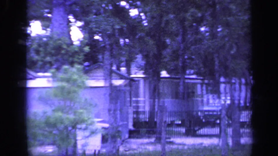 1968 Florida 8mm view of pine trees, a low camp building, fencing, and shaded cabin grounds.