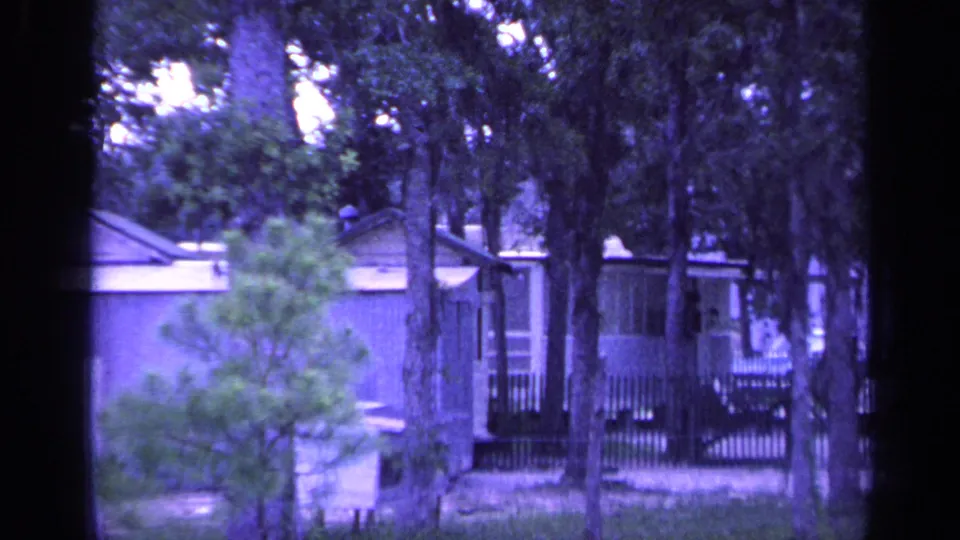 Florida camp cabin exterior in 1968, framed by pine trees, fencing, and a shaded dirt clearing on 8mm film.