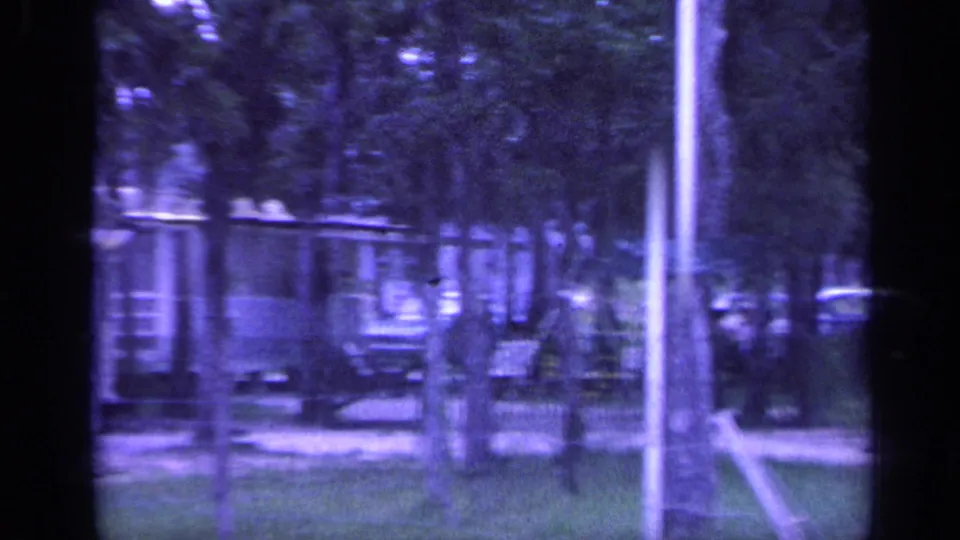 1968 Florida home-movie frame showing a shaded park area with trees, parked cars, a pole, and distant recreational structures.