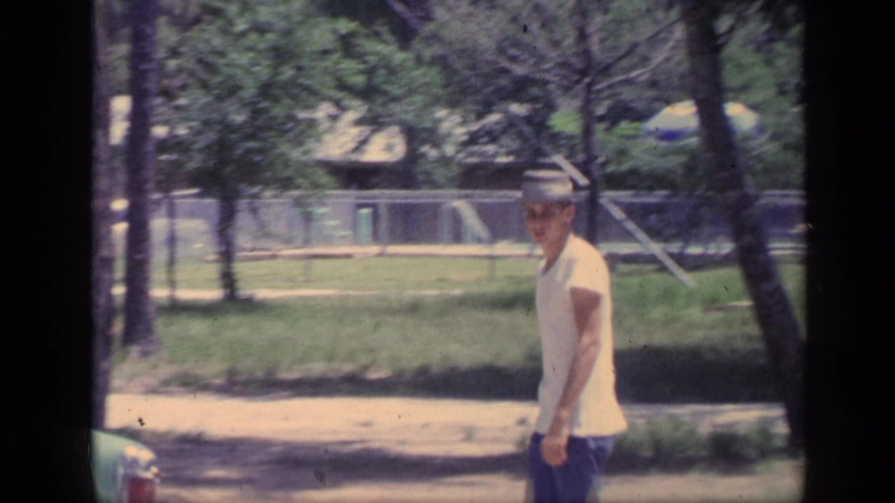 Young man in a brimmed hat walks along a park path among trees.