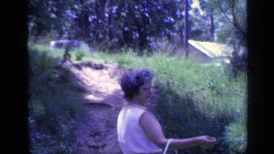 A woman in a light dress carries a purse along a wooded Florida path in this 1968 home-movie frame.