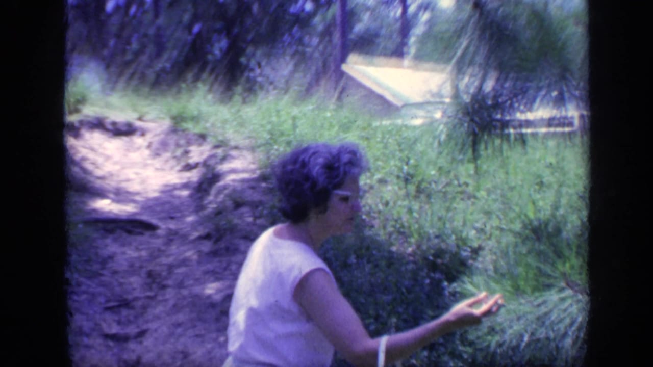 Woman in a white sleeveless dress pauses beside greenery on a dirt path.