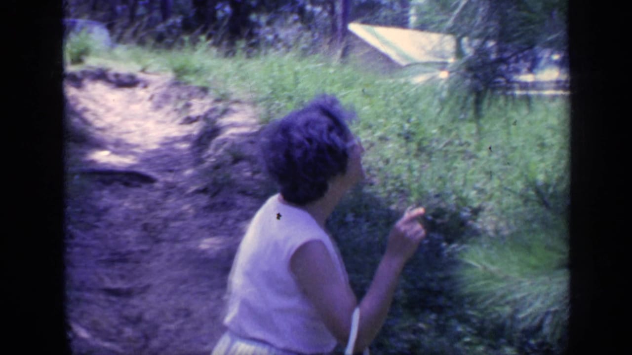 The woman faces the greenery beside the path, her short hair and glasses partly visible in the 1968 Florida scene.