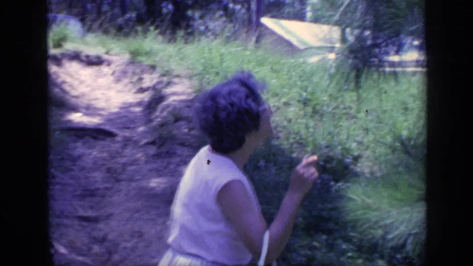 The woman faces the greenery beside the path, her short hair and glasses partly visible in the 1968 Florida scene.