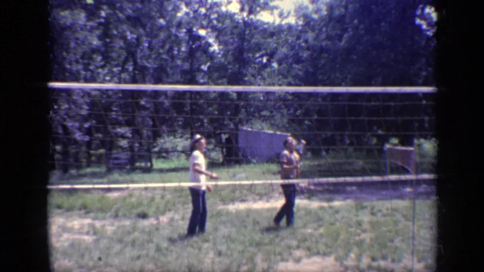 Two young men play badminton across a portable net in a wooded Florida yard, consistent with the 1968 home-movie metadata.