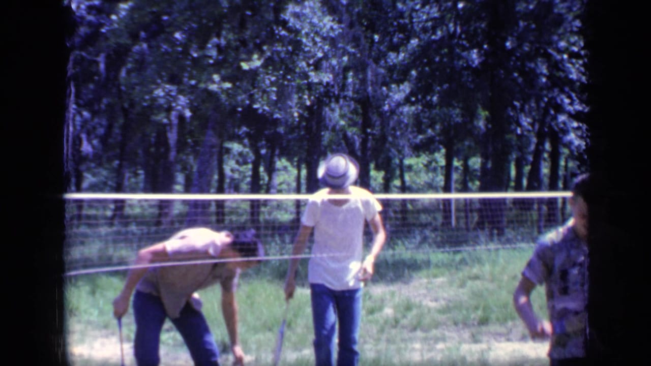 A man bends near the badminton net while another player stands nearby.