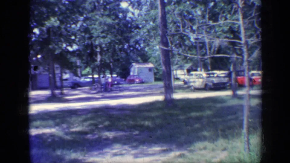 A wooded Florida campground scene from 1968 shows parked cars, grass, trees, and distant people near a small structure.