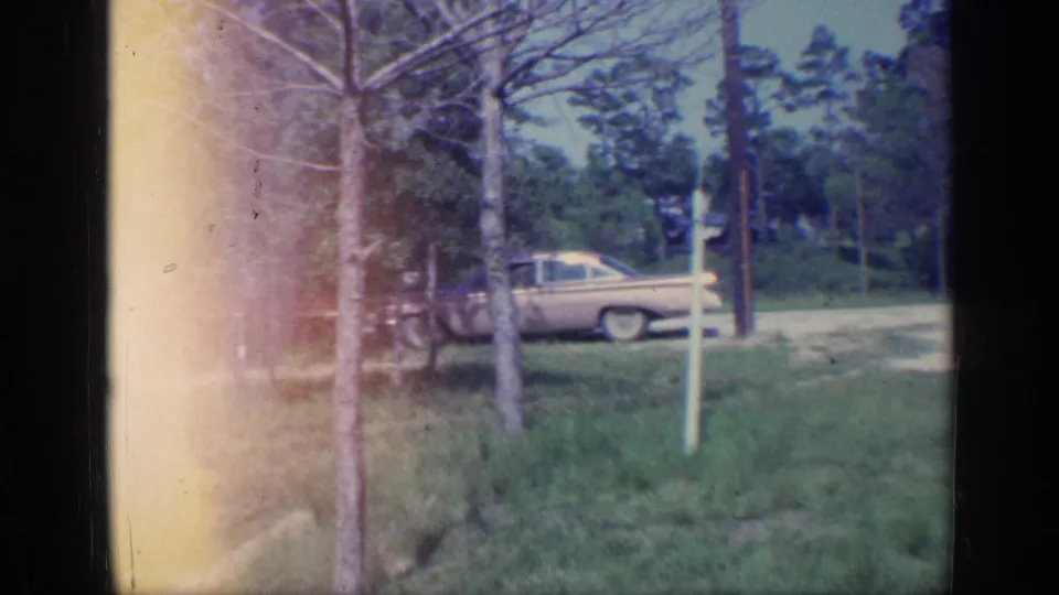 1968 Florida 8mm frame showing a pale car near the roadside, partly framed by trees, grass, and a bright exposure flare.