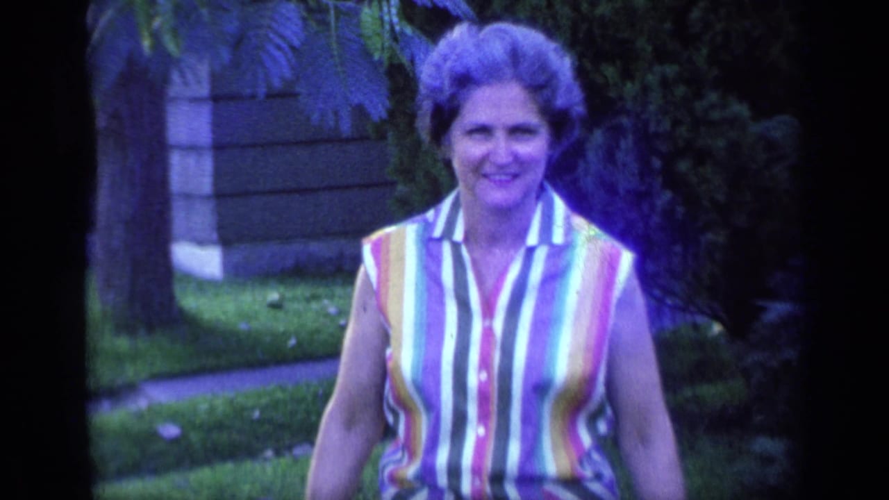 Woman in a striped sleeveless top walks toward the camera on a lawn.