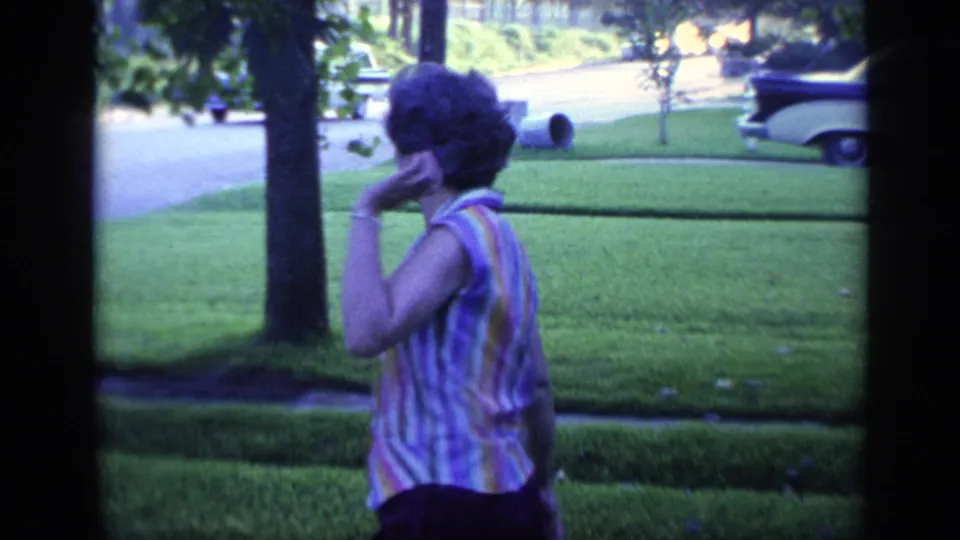 Woman in a striped sleeveless top turns in profile on a Florida lawn, with trees, street, and parked cars in view.
