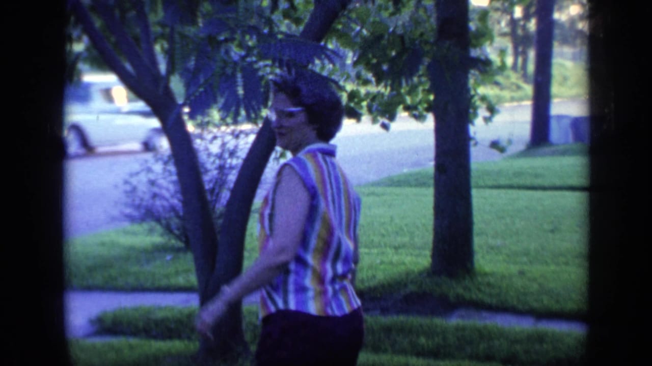 Woman in glasses turns toward the camera beside trees in a front yard.