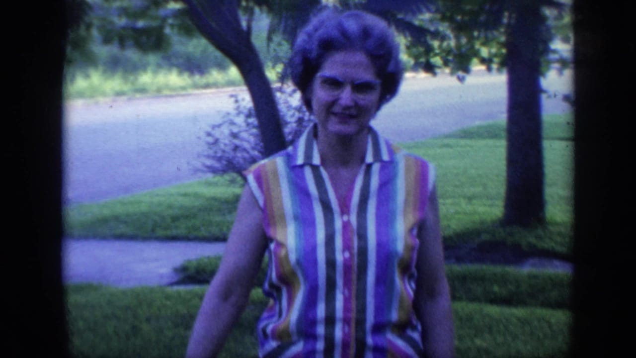 Woman in a striped sleeveless shirt walks across a green suburban yard toward the camera.